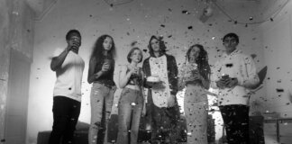 Group of friends celebrating indoors with confetti and balloons in a black and white setting.