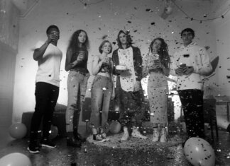 Group of friends celebrating indoors with confetti and balloons in a black and white setting.