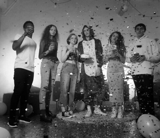 Group of friends celebrating indoors with confetti and balloons in a black and white setting.
