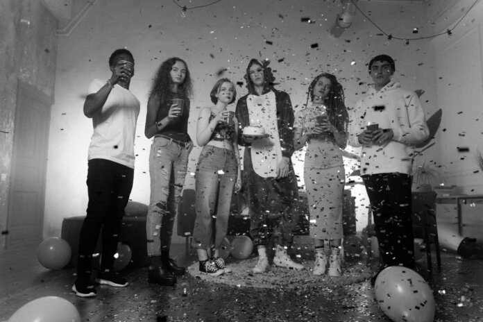 Group of friends celebrating indoors with confetti and balloons in a black and white setting. Group of friends celebrating indoors with confetti and balloons in a black and white setting.