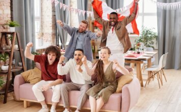 Group of friends cheering indoors with a Canadian flag, enjoying a lively moment together.