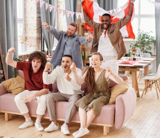 Group of friends cheering indoors with a Canadian flag, enjoying a lively moment together.