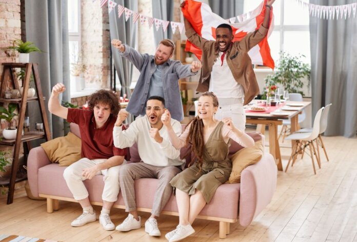 Group of friends cheering indoors with a Canadian flag, enjoying a lively moment together.
