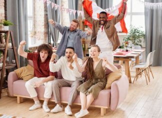 Group of friends cheering indoors with a Canadian flag, enjoying a lively moment together.