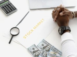 Hands folded over stock market documents with calculator and cash on desk.