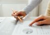 Hands holding a pencil, analyzing charts and data sheets, suggesting teamwork in an office setting.