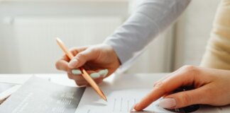 Hands holding a pencil, analyzing charts and data sheets, suggesting teamwork in an office setting.