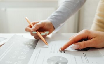 Hands holding a pencil, analyzing charts and data sheets, suggesting teamwork in an office setting.