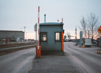 Пограничная служба изъяла более полутонны опиума, спрятанного в бумаге Industrial checkpoint and barrier at port under cloudy sky with cranes in the background.