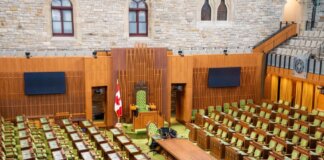 Interior view of the Canadian House of Commons with green seating and wooden decor.