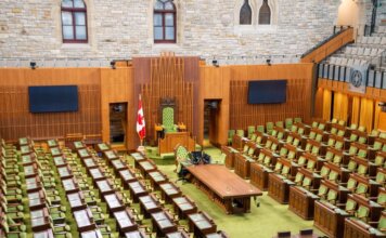 Interior view of the Canadian House of Commons with green seating and wooden decor.