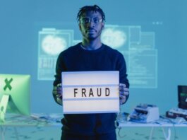 Man holding a 'FRAUD' sign in a tech setting, symbolizing cybersecurity threats.