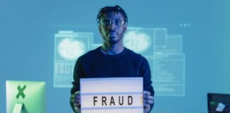 Man holding a 'FRAUD' sign in a tech setting, symbolizing cybersecurity threats.