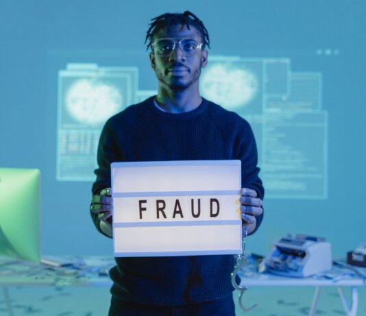 Man holding a 'FRAUD' sign in a tech setting, symbolizing cybersecurity threats.