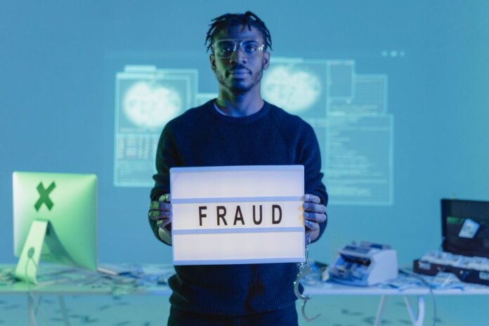 Man holding a 'FRAUD' sign in a tech setting, symbolizing cybersecurity threats. Man holding a 'FRAUD' sign in a tech setting, symbolizing cybersecurity threats.