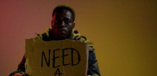 Man with a cardboard sign seeking employment, highlighting unemployment and social issues.