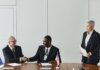 Multinational business meeting with agreement signing, featuring diverse professionals and flags.
