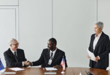 Multinational business meeting with agreement signing, featuring diverse professionals and flags.