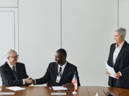 Multinational business meeting with agreement signing, featuring diverse professionals and flags.
