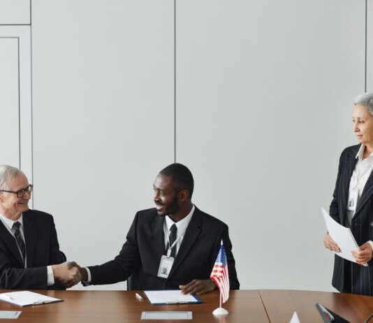 Multinational business meeting with agreement signing, featuring diverse professionals and flags.