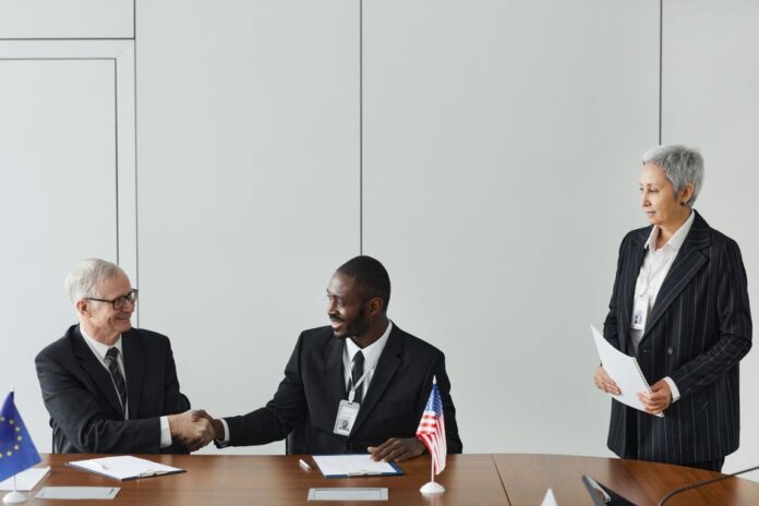 Multinational business meeting with agreement signing, featuring diverse professionals and flags. Multinational business meeting with agreement signing, featuring diverse professionals and flags.