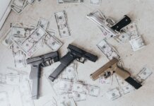 Полиция разыскивает подозреваемого в ограблении банка в Берлингтоне Multiple firearms and US dollar bills scattered on a floor in a high-angle view.