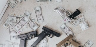 Multiple firearms and US dollar bills scattered on a floor in a high-angle view.