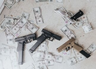 Полиция разыскивает подозреваемого в ограблении банка в Берлингтоне Multiple firearms and US dollar bills scattered on a floor in a high-angle view.