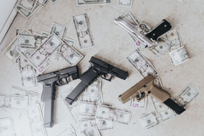 Multiple firearms and US dollar bills scattered on a floor in a high-angle view.
