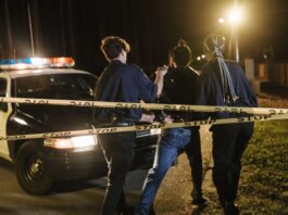 Nighttime arrest scene with police officers and patrol car behind caution tape.