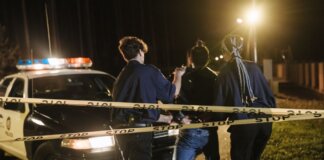 Nighttime arrest scene with police officers and patrol car behind caution tape.