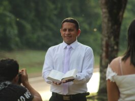 Pastor conducts a ceremony outdoors holding an open book with wedding participants.