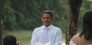 Pastor conducts a ceremony outdoors holding an open book with wedding participants.