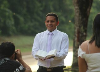 Pastor conducts a ceremony outdoors holding an open book with wedding participants.