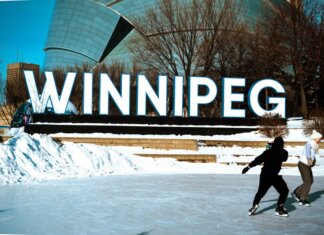 People ice skating in front of the iconic Winnipeg sign on a sunny winter day.
