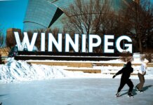 People ice skating in front of the iconic Winnipeg sign on a sunny winter day.