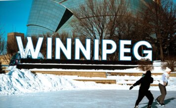 People ice skating in front of the iconic Winnipeg sign on a sunny winter day.