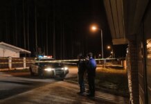 Женщина ранена ножом при ночном вторжении в дом в Лондоне, Онтарио Police officers at a nighttime crime scene with a police car and caution tape under streetlights.