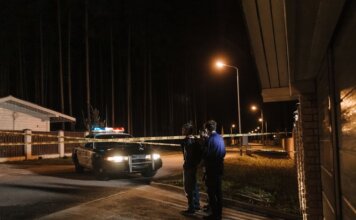 Женщина ранена ножом при ночном вторжении в дом в Лондоне, Онтарио Police officers at a nighttime crime scene with a police car and caution tape under streetlights.