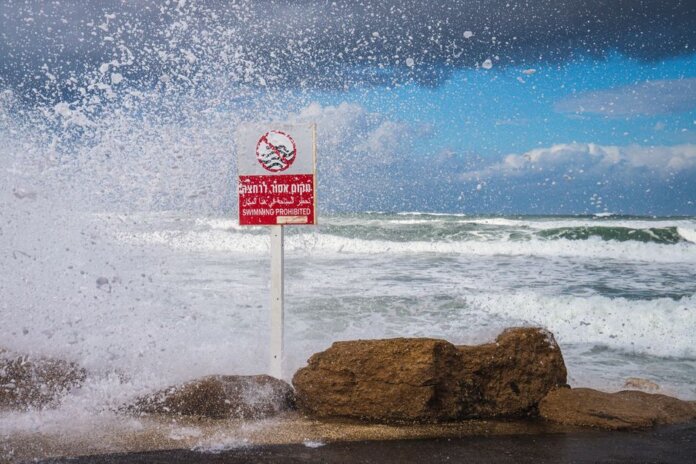 Powerful waves crash against the rocks with 'Swimming Prohibited' sign in Tel Aviv beach scene. Powerful waves crash against the rocks with 'Swimming Prohibited' sign in Tel Aviv beach scene.