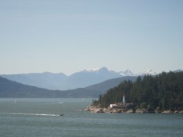 Serene landscape of a lighthouse by the sea with mountains in the background.