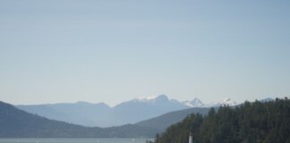 Serene landscape of a lighthouse by the sea with mountains in the background.