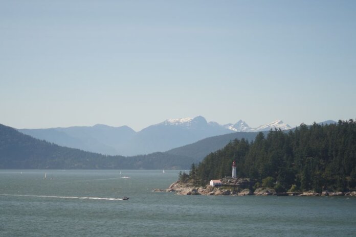 Serene landscape of a lighthouse by the sea with mountains in the background.