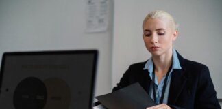 Serious young woman in formal clothes sitting at table and working with documents in office