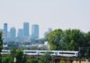 Skyline of Warsaw with modern buildings and a train passing amidst the greenery.