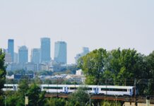 Skyline of Warsaw with modern buildings and a train passing amidst the greenery.