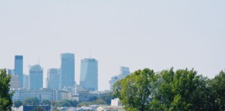 Skyline of Warsaw with modern buildings and a train passing amidst the greenery.