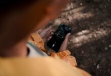 Teenage boy holds a smartphone displaying low battery outdoors in a forest.