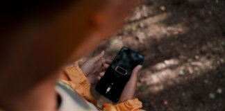 Teenage boy holds a smartphone displaying low battery outdoors in a forest.