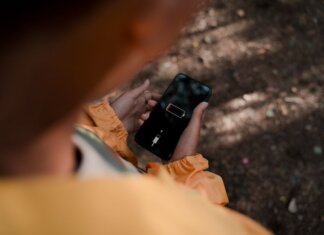 Teenage boy holds a smartphone displaying low battery outdoors in a forest.